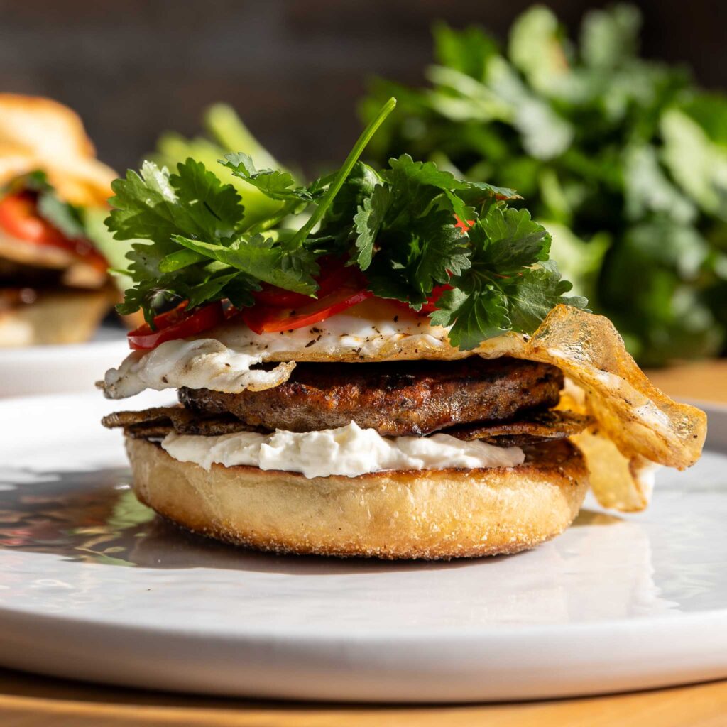 breakfast sandwich on plate with bun, sausage, egg, peppers, herbs