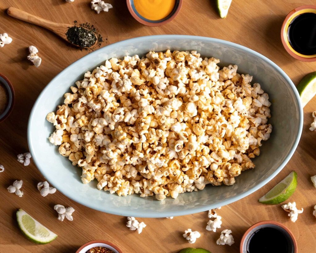 Popcorn in a bowl surrounded by sauces and limes